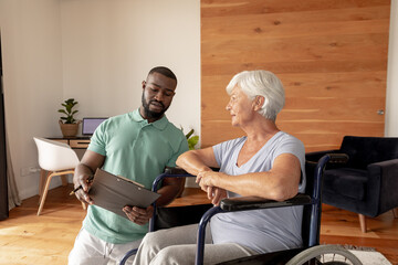 African american male physiotherapist with clipboard discussing with senior woman on wheelchair