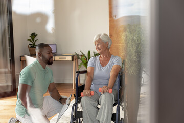 Obraz premium African american male physiotherapist helping caucasian senior woman to do exercise with dumbbells