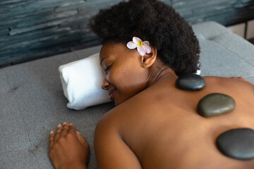 African american woman woman with eyes closed receiving hot stone massage at home - Powered by Adobe