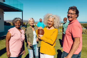 Portrait of happy multiracial senior friends playing rugby in yard against clear sky at nursing home