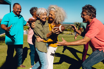 Cheerful multiracial senior friends playing rugby in yard against clear blue sky on sunny day