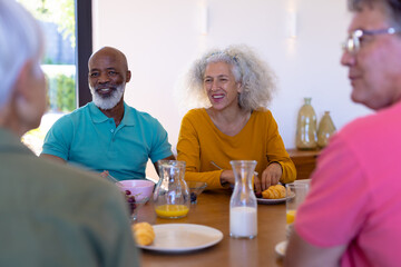Fototapeta na wymiar Happy multiracial senior friends talking while having breakfast at dining table in retirement home