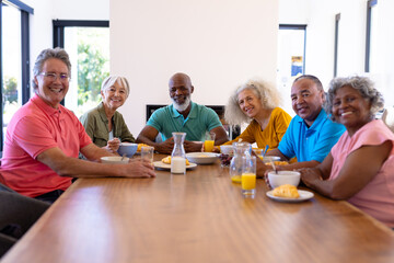 Portrait of happy multiracial senior friends with food and drink on dining table in nursing home