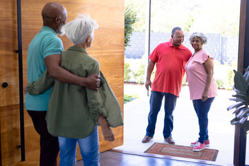 Multiracial seniors welcoming friends while standing at open entrance in retirement home