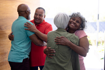 Multiracial seniors embracing and welcoming friends while standing at doorway in nursing home