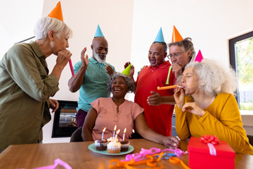 Multiracial senior friends singing and blowing party horns for senior woman in nursing home - Powered by Adobe