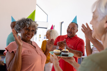 Cheerful multiracial seniors clapping and singing for senior woman while celebrating birthday