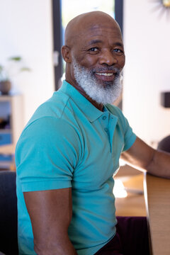 Portrait Of Smiling African American Bald Senior Man Sitting At Dining Table In Nursing Home