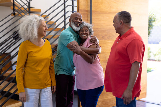 Happy multiracial seniors welcoming friends while standing at doorway in retirement home - Powered by Adobe