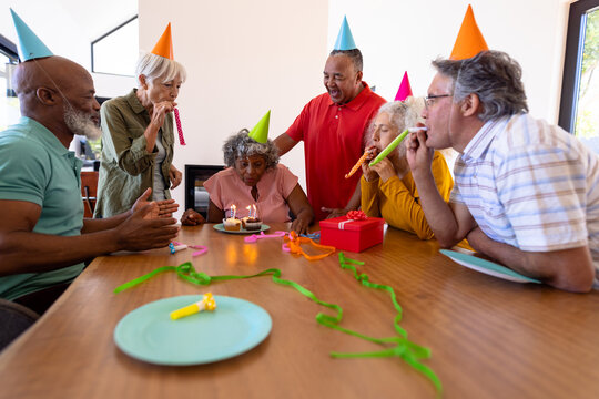 Multiracial senior friends blowing party horns while senior woman blowing birthday candles