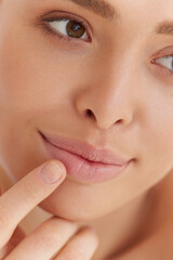 Lips skin care. Beautiful caucasian woman with natural makeup touching with finger her full lips...