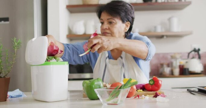 Asian senior woman putting the skins of vegetables in the compost bin in the kitchen