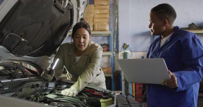 Video of two diverse female car mechanics talking, using laptop and repairing car