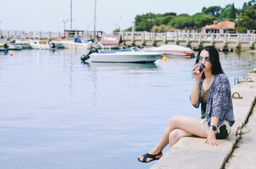 Fototapeta na wymiar Lifestyle Portrait. Beautiful happy woman walking, relaxing, enjoying in sunny day at beach. Summer. Drinking coffee. Adriatic Sea