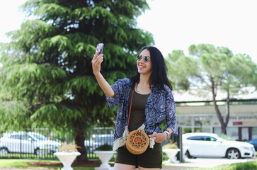 Portrait of young happy business woman relaxing, working in green park in city. Using phone. Selfie. Technology. Social media. Video call