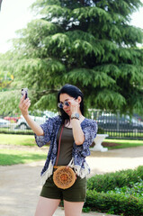 Fototapeta premium Portrait of young happy business woman relaxing, working in green park in city. Using phone. Selfie. Technology. Social media. Video call