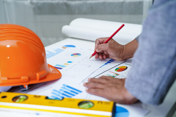 Architect or engineer working project accounting with graph and construction helmet in office,...