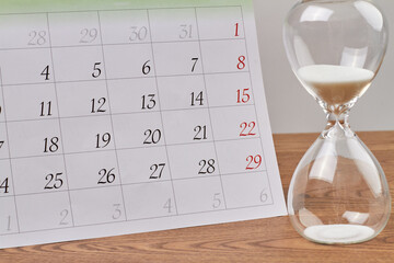 Close-up hourglass and month calendar on wooden desk. Sandglass countdown timer.