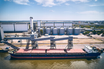 Bulk carrier ship in cargo port. Aerial view of barge in a dock. Grain elevator and granary silos at background. 
