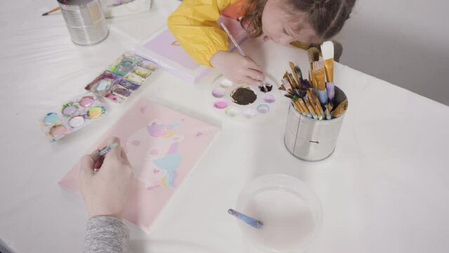 Little girl painting with acrylic paint on canvas with her mother for a distant learning art project.