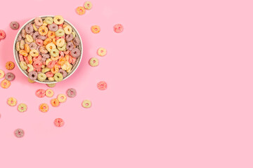 Cereales de maíz coloridos en forma de anillo dentro de un cuenco sobre un fondo rosa pastel liso...