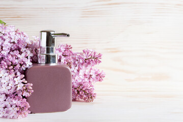Bathroom dispenser and lilac inflorescences. Concept for spa, beauty and health salon, cosmetics store. Close up photo on white wooden background.