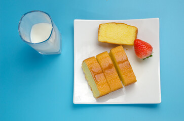 Blue background and white milk in glass, cake in white plate