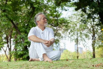 Fototapeta premium An Asian senior man in white is relaxing on the garden lawn. rest, exercise, sitting Meditation, health care, mind in the garden. man with meditation in park