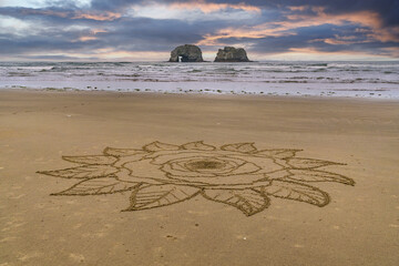 Intricate mandala star sand design on the ocean beach with Twin Rocks in the ocean and beautiful...