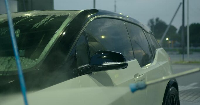 Woman with a hose with water in her hands washes the car