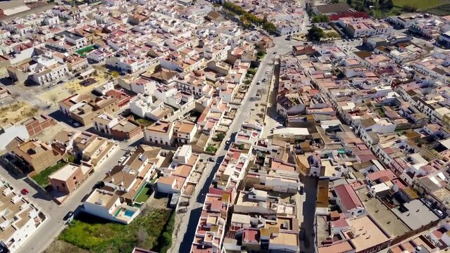 drone wide angle tilting view  of a wonderful white town of Cadiz, Spain with its colored roofs and in the background the green summer fields with vineyards and different green and yellow colors