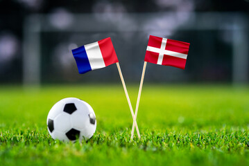 Fototapeta premium France vs. Denmark, Stadium 974, Football match wallpaper, Handmade national flags and soccer ball on green grass. Football stadium in background. Black edit space.
