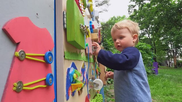A happy child plays with educational toys in the playground in summer. Wooden game board. Copy space - entertainment concept, bright board for children, kindergarten, fine motor skills of fingers