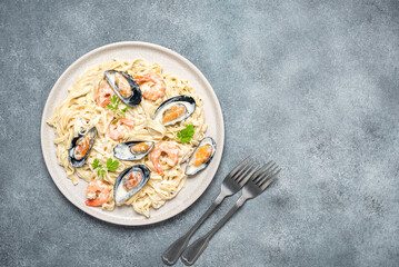 Fettuccine pasta in a creamy sauce with seafood in a plate on a gray concrete background. Pasta with shrimps and mussels. Top view, flat lay.
