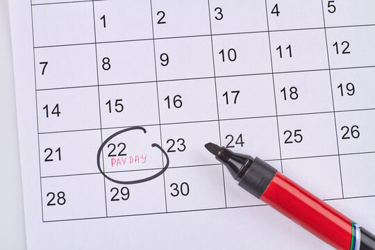 Marking pay day in the white paper calendar top view. Black non-toxic marker.