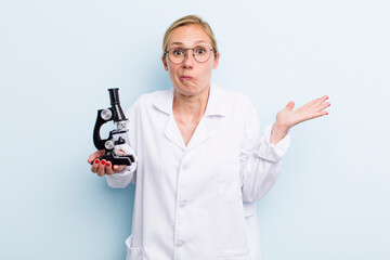 young adult blonde woman feeling puzzled and confused and doubting. scientist with a microscope...