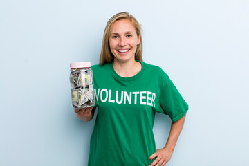 young adult blonde woman smiling happily with a hand on hip and confident. volunteer and donation...