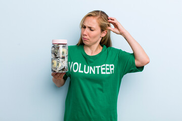 young adult blonde woman smiling happily and daydreaming or doubting. volunteer and donation concept
