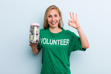 young adult blonde woman feeling happy, showing approval with okay gesture. volunteer and donation...