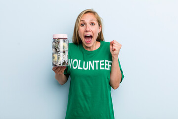 young adult blonde woman feeling shocked,laughing and celebrating success. volunteer and donation...