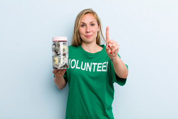 young adult blonde woman smiling and looking friendly, showing number one. volunteer and donation...