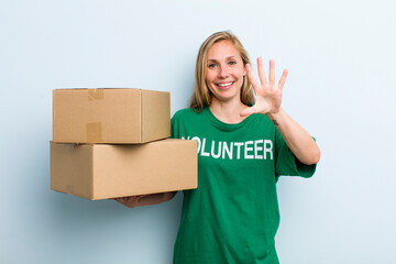 young adult blonde woman smiling and looking friendly, showing number five. volunteer and donation...