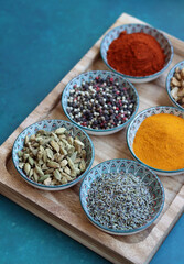 Oriental bowls with various Indian spices on wooden tray. Aromatic spices and herbs close up photo. Paprika, pepper, cardamom, turmeric, lavender. 