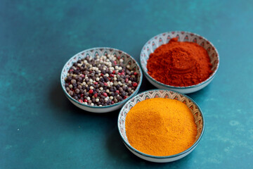Three small ceramic bowls with peppercorns, paprika and turmeric powder. Simple composition still life with aromatic Indian spices. Healthy eating concept. 