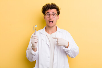 young handsome guy looking shocked and surprised with mouth wide open, pointing to self. dentist...