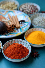 Close up photo of spices and herbs in blue ceramic bowls. Paprika, turmeric, anise, lavender, cardamom, cinnamon, pepper on textured blue background. 