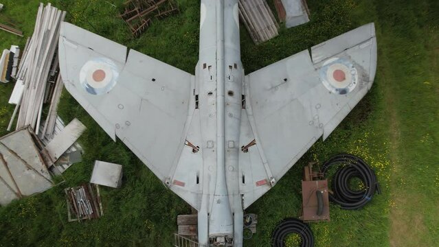 Rising aerial view above wings of distressed Hawker hunter fighter aircraft on British renovation farmland yard