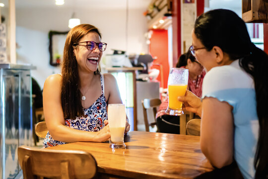 latina women, mother and daughter in a restaurant laughing, drinking juice