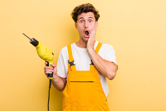 young handsome guy feeling shocked and scared. handyman with a drill concept