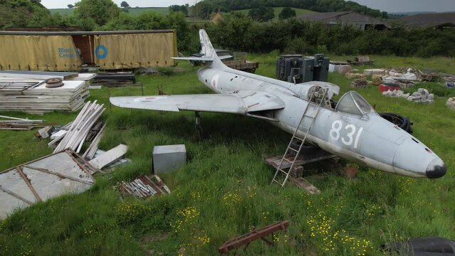 Scrap Hawker hunter air force fighter jet among junk in overgrown farmland pasture